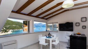 A modern kitchen with a dining area, large windows with a view of the sea, and a TV mounted on the wall. - Mali Skoj Apartment - Two-Bedroom Apartment with Sea View (Sudurad)