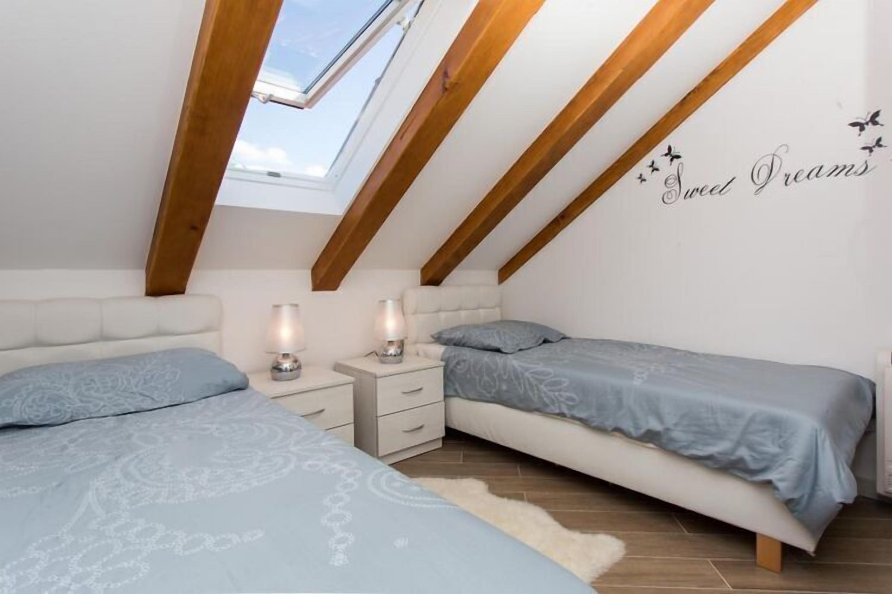 A bedroom with two beds, a skylight, and a 'Sweet Dreams' wall decal.