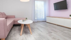 Ein modernes Wohnzimmer mit einem rosafarbenen Sofa, einem weißen runden Tisch und einem an der Wand befestigten Fernseher.