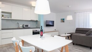 A modern kitchen with white cabinets, a microwave, and a wine bottle on the counter. There is a dining table with chairs and a sofa in the living area. - Apartments Dva Galeba - One Bedroom Apartment with Sea View (206) (Bol)