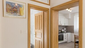 A hallway leading to a kitchen with wooden doors, a framed painting on the wall, and a dining area with a chair. - Villa Celenca - Two Bedroom Apartment with Terrace and Pool View - A1 (Mokosica)