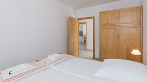 A bedroom with a bed, a wooden wardrobe, a nightstand with a lamp, and a door leading to a bathroom. - Villa Celenca - Two Bedroom Apartment with Terrace and Pool View - A1 (Mokosica)
