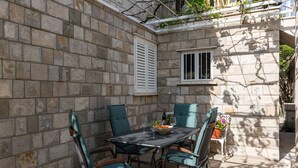 Eine Terrasse mit Steinmauern, einem Tisch, Stühlen, einem Fenster und einem Blumentopf.