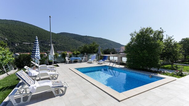 Ein Swimmingpool mit Liegestühlen und Sonnenschirmen, umgeben von Grünflächen und Hügeln.