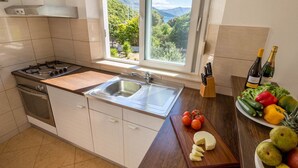 Una cocina con estufa a gas, lavamanos y ventana con vistas a zonas verdes y montañas.