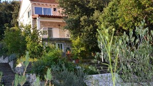 Una casa de dos pisos con balcón, rodeada de exuberante vegetación y escalones de piedra.