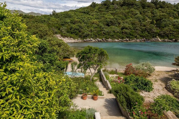 A coastal landscape with a clear view of a beach, a small pool, and lush greenery.