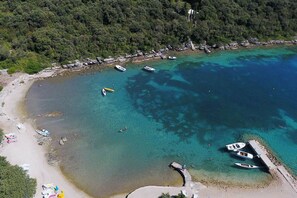 A coastal area with boats docked near the shore, a sandy beach, and a forested hillside in the background.