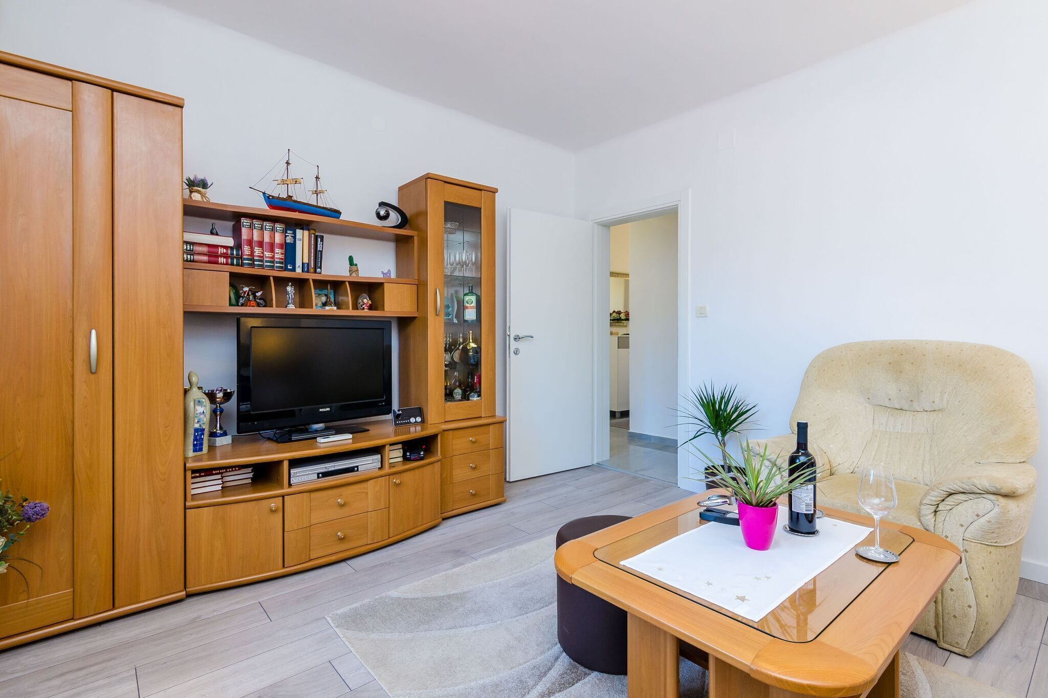 Un soggiorno con un mobile TV in legno, televisore e una poltrona beige.
