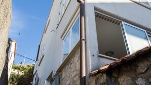 Una calle estrecha con un edificio de fachada de piedra y una ventana con canalón metálico.