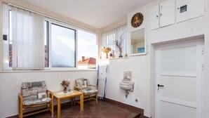 Una habitación con dos sillas, una mesita, una ventana con persianas, una puerta blanca y un espejo fijado a la pared.