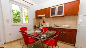 Una cocina moderna con armarios de madera, una mesa de comedor de vidrio y sillas rojas, además de un refrigerador blanco.