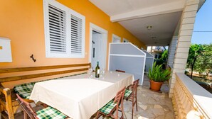 Un área de comedor al aire libre techada, con una mesa dispuesta para dos, bancos de madera con cojines a cuadros, una planta en maceta y un suelo de piedra.