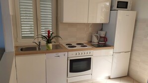 Una cocina compacta con muebles blancos, horno empotrado, microondas y cafetera.