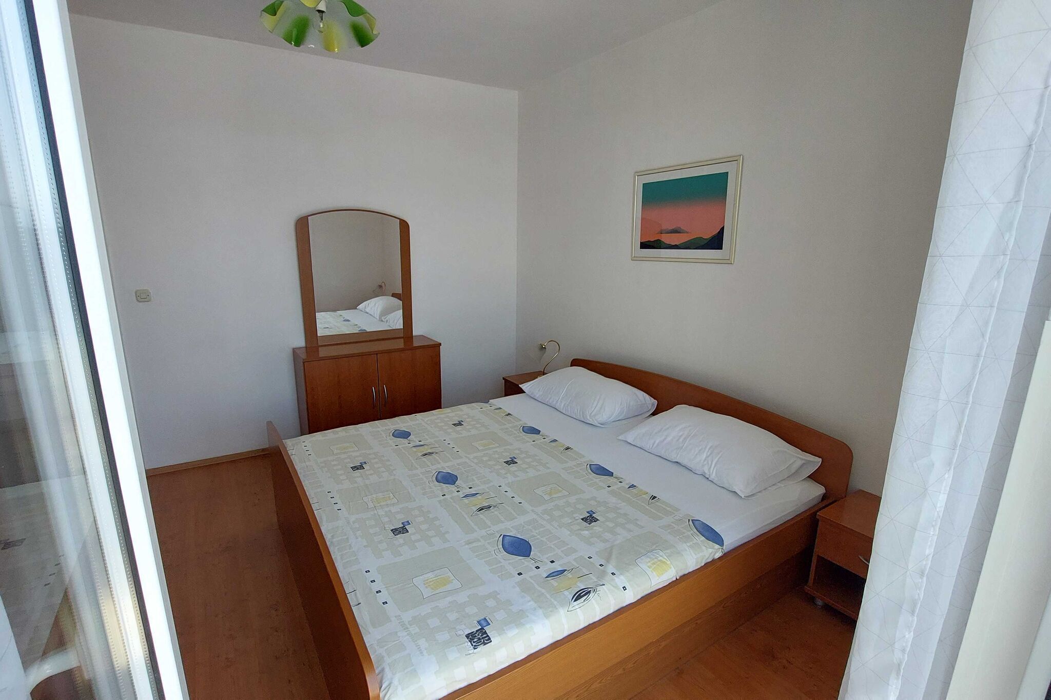 Une chambre à coucher avec un lit, une table de chevet, une armoire en bois, un miroir et un tableau accroché au mur.