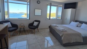 A hotel room with a bed, two chairs, a desk, a TV, and large windows with a view of the sea. - Apartments Matea - Studio with Sea View (2 Adults) - (Štikovica) (Stikovica)