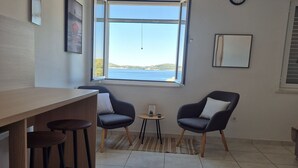 A room with a large window, a wooden table, two chairs, and a small round table with a clock on the wall. - Apartments Matea - Studio with Sea View (2 Adults) - (Štikovica) (Stikovica)