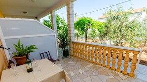 A covered outdoor dining area with a table set for two, potted plants, and a view of the surrounding garden. - Apartments Ivana (TR) -Studio with Terrace ( A2) (Trogir)