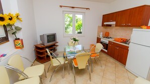 A compact kitchen with a dining area, wooden cabinets, a television, and a window with a view of greenery. - Apartments Ivana (TR) - One Bedroom Apartment with Terrace (A3) (Trogir)