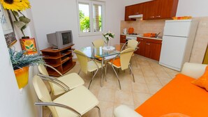 A compact kitchen with a dining area, including a glass table and chairs, a refrigerator, and wooden cabinets. - Apartments Ivana (TR) - One Bedroom Apartment with Terrace (A3) (Trogir)