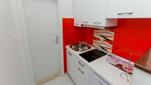 Une cuisine de taille réduite avec des meubles blancs, un crédence rouge et une machine à café.