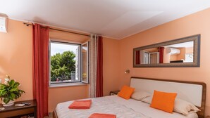 A bedroom with a bed, a nightstand, a mirror, and a window with curtains.