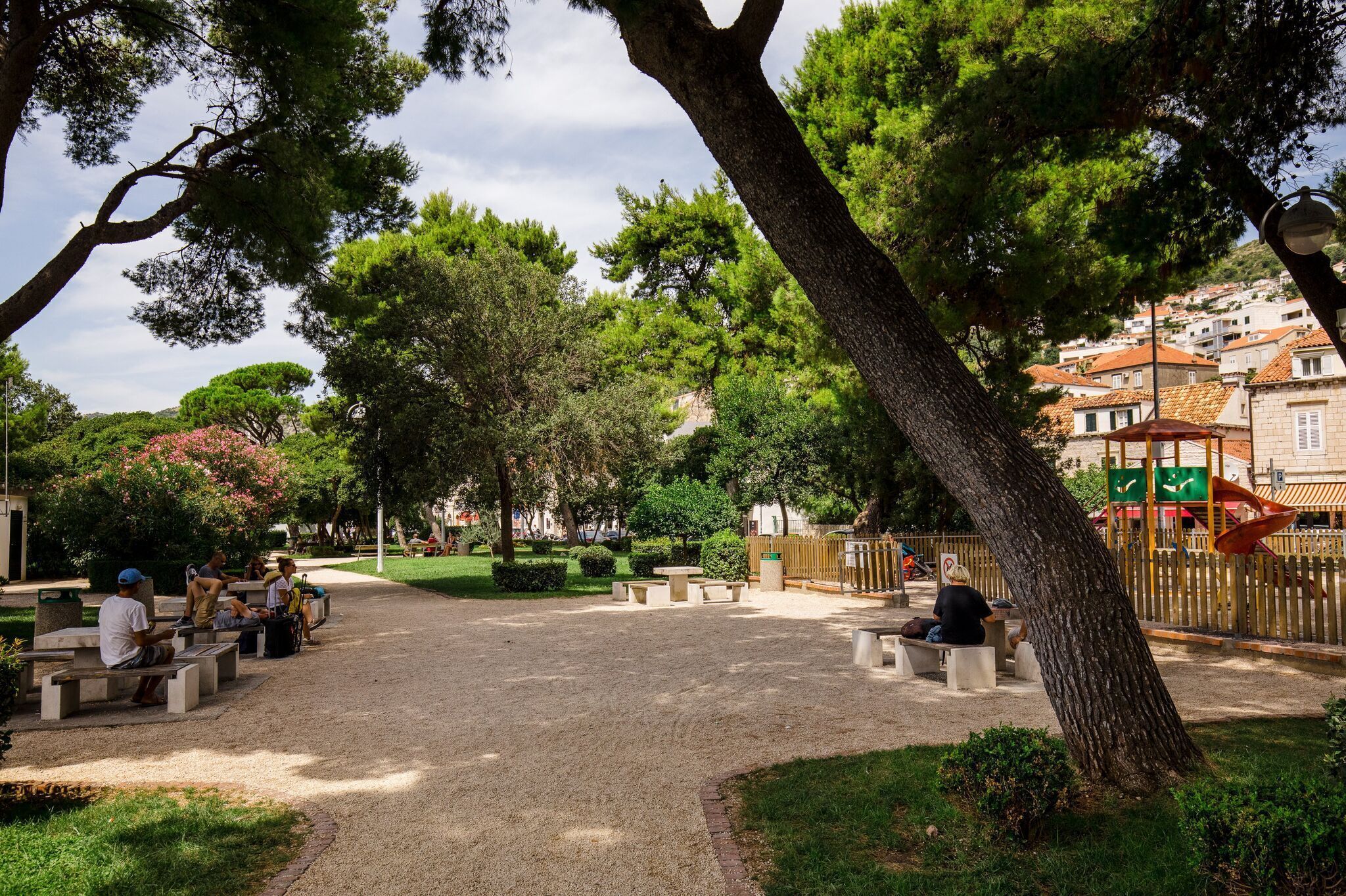 Ein Park mit Bänken und Picknicktischen, umgeben von Bäumen und einem Spielplatz.