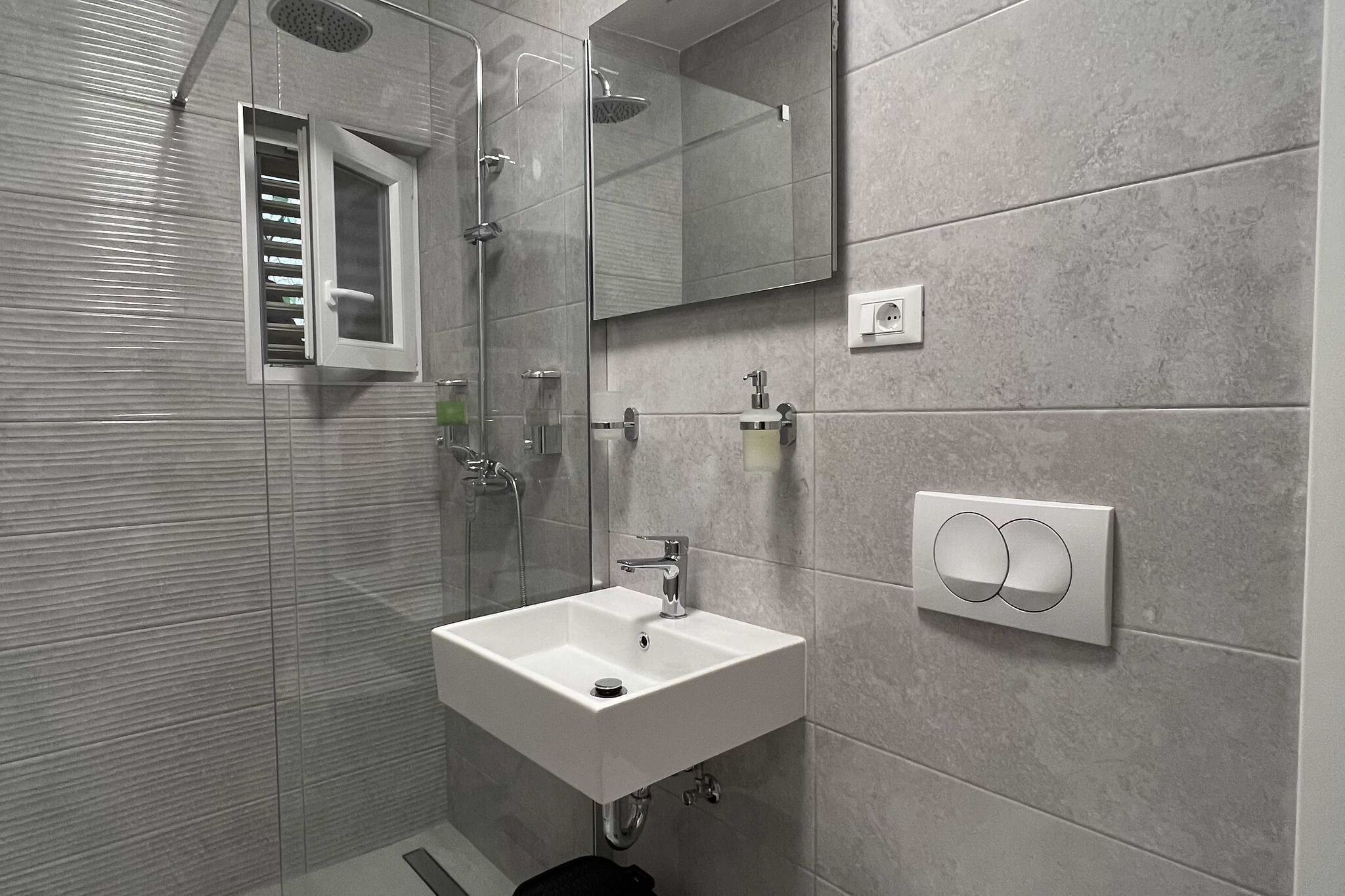 Ein modernes Badezimmer mit einer Duschkabine aus Glas, einem weißen Waschbecken und einem Spiegel.