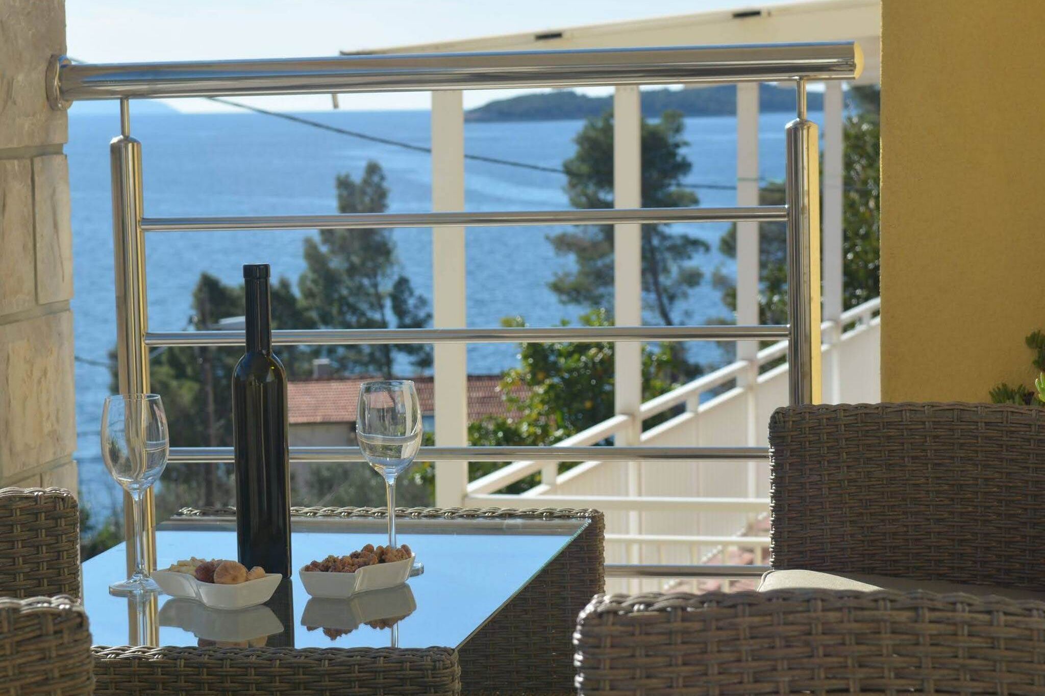 Ein Balkon mit Korbmöbeln, einem Glastisch, zwei Weingläsern, einer Flasche und einer Nuss-Schale.