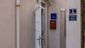 Ein schmaler Gang mit einer weißen Tür, einem blauen Schild mit der Zimmernummer 1 und einer braunen Verteilerdose.
