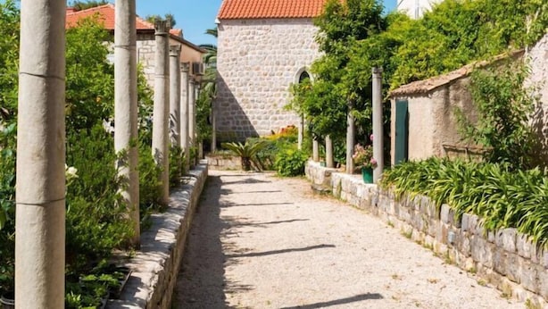 A narrow cobblestone street flanked by stone buildings and greenery.