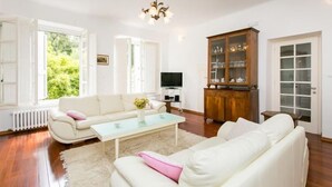 A living room with a white sofa, a glass coffee table, a wooden cabinet with glass doors, and a television.
