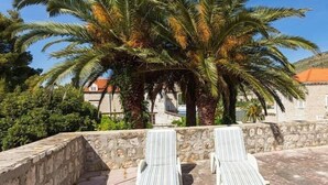 A stone wall with two white lounge chairs and a palm tree.