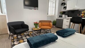 A compact living space with a sofa, a chair, a small table with flowers, a TV, and a kitchenette. - Apartments Noa Old Town - Studio - First Floor (Dubrovnik)