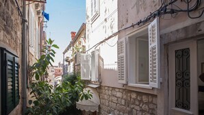 A narrow street with stone buildings, white shutters, and a small tree. - Apartments Noa Old Town - Studio - First Floor (Dubrovnik)