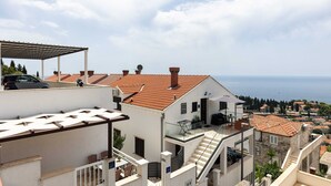 Zona residenziale caratterizzata da tetti in tegole di terracotta, un edificio bianco con un balcone e vista sul mare.