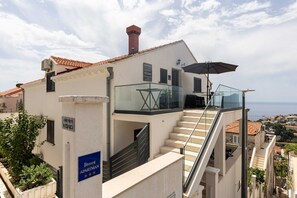 A building with a sign indicating 'Apartments KONO' and a staircase leading to a balcony with a glass railing.