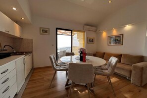 A modern kitchen with a dining area, a sofa, and a view through a glass door.