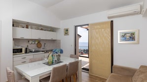 Cocina moderna con armarios blancos, una mesa de comedor y sillas. Se ve el exterior a través de una puerta de vidrio.
