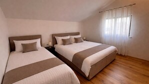 Una habitación con dos camas, piso de madera y ventana con cortinas.