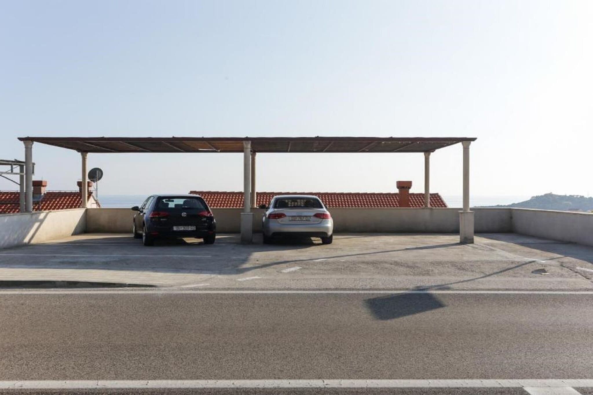Zona aparcament amb dos cotxes, una estructura coberta i vistes al mar.
