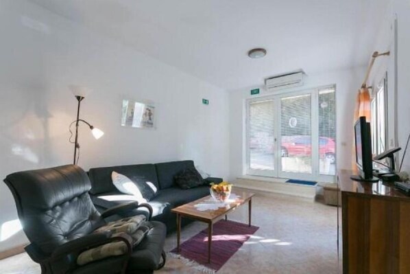 A modern living room with a leather sofa, a wooden coffee table, and a glass door leading outside. - Apartment Anita (Gruž) - One-Bedroom Apartment with Balcony (Dubrovnik)