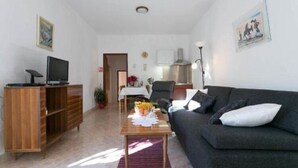 A living room with a dark grey sofa, a wooden entertainment unit, and a small table with a vase of flowers. - Apartment Anita (Gruž) - One-Bedroom Apartment with Balcony (Dubrovnik)