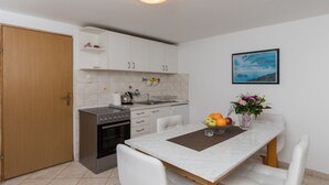 A compact kitchen with a stove, oven, and white cabinets. There's a dining table with chairs and a vase with flowers.