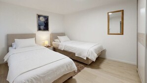 A hotel room with two beds, a nightstand, a bedside lamp, a framed picture on the wall, and a mirror.