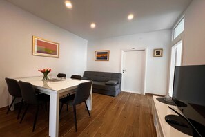 Uma sala de estar moderna com mesa de jantar, sofá, TV e obras de arte nas paredes.