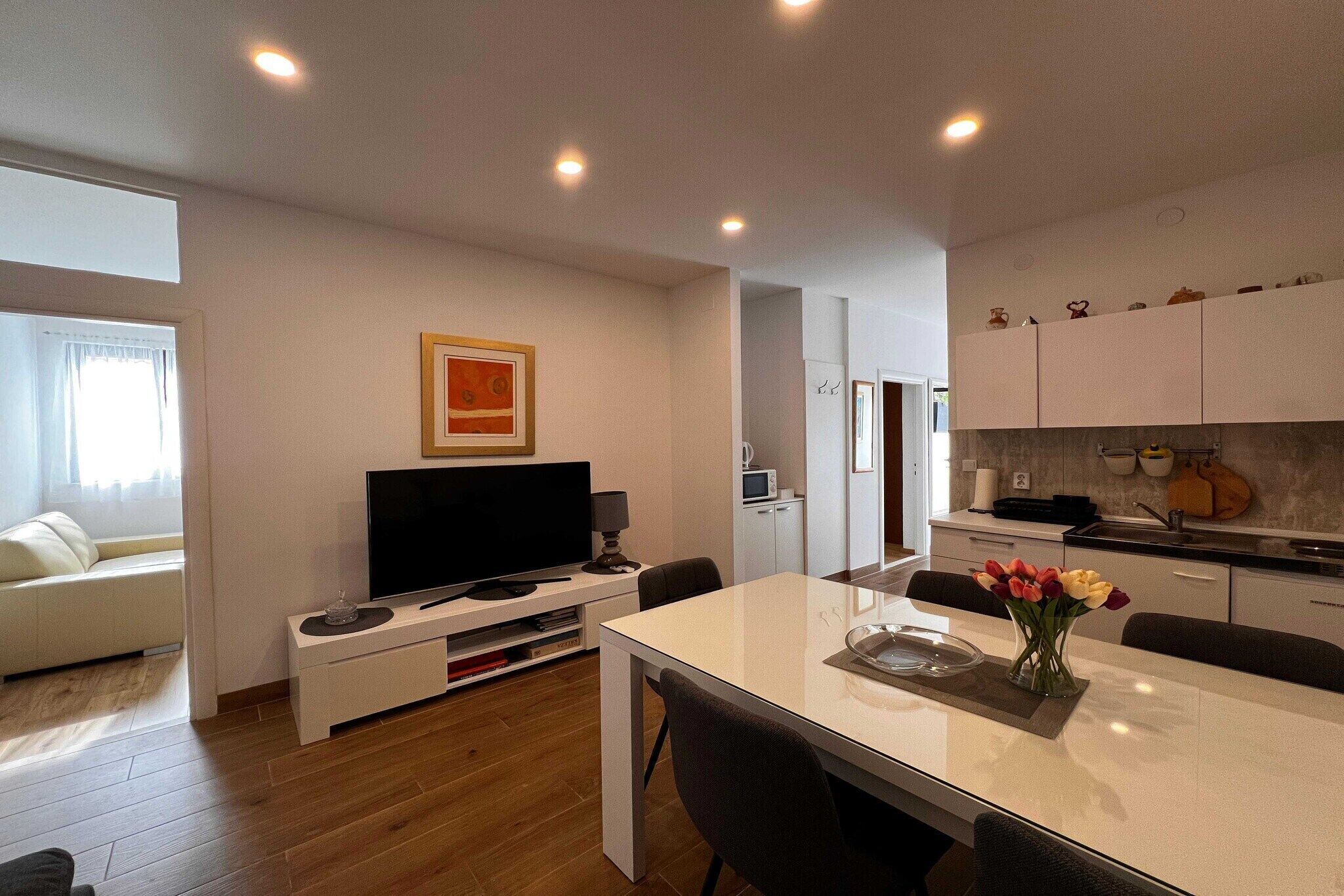 Una sala moderna con una televisión de pantalla plana, una mesa de comedor con sillas, un sofá y una cocina con armarios y electrodomésticos.