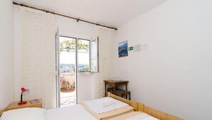 Une chambre avec deux lits, un bureau, une chaise, une lampe rouge et une vue sur l’extérieur.