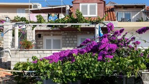 A residential building with stone walls, white shutters, and a balcony with a red-tiled roof.