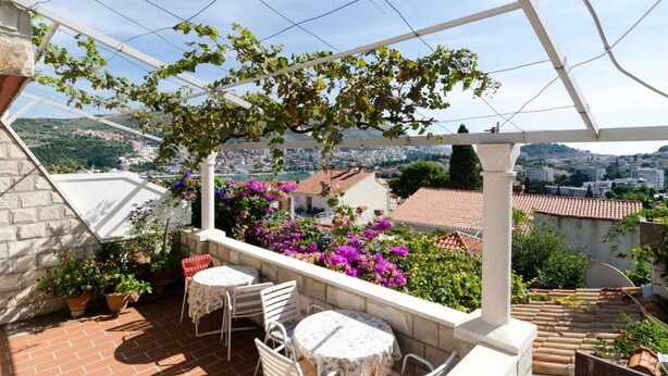 A terrace with a pergola, potted plants, and a table and chairs.